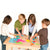 A group of 4 children standing around a table putting together the Asia Geo Puzzle. A dark-haired girl on the left, then a blonde boy to her right, then a dark-haired girl to his right, and a dark-blonde boy to her right. On the table, the right portion of the puzzle is put together with the other pieces scattered along the table. The country pieces are rec, orange, yellow, green, and pink with blue ocean pieces.