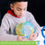 A black-haired boy sitting at a table putting together the Puzzleball Globe. The 3 D globe is mostly finished while he is holding it up and putting 2 pieces together. There are pieces and the stand sitting on the table in front of him.