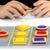 A close-up of a boys’ hands playing with the Smart Cookies game. He is holding a blue triangle with both hands. The game board in front of him is filled with the red, yellow, and blue cookie pieces that are triangle, circle, and square shaped.