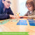A customer photo of an mom and a daughter playing Tiny Polka Dots on a table. The mom on the left is pointing to a card and the daughter has her hands out and is pointing to a dot on one of the cards. There are many cards laid out on the table, face up. Between them is the game box propped up, so you can read the title.